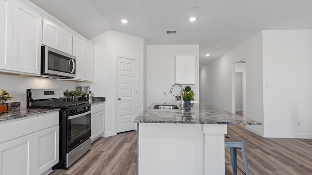 kitchen with sink, dark stone countertops, white cabinets, a kitchen island with sink, and stainless steel appliances