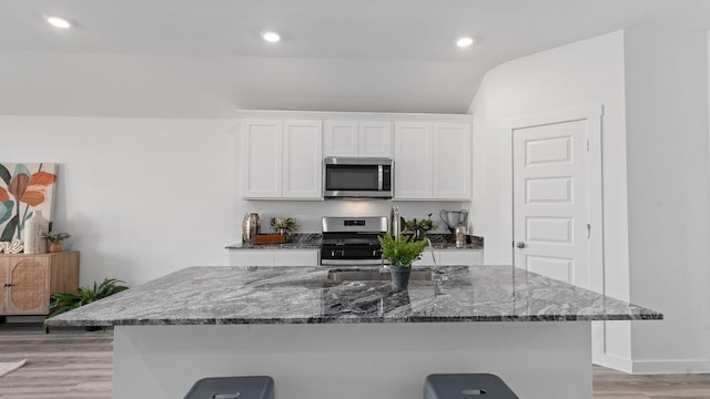 kitchen with stainless steel appliances, a breakfast bar, white cabinets, and a center island with sink