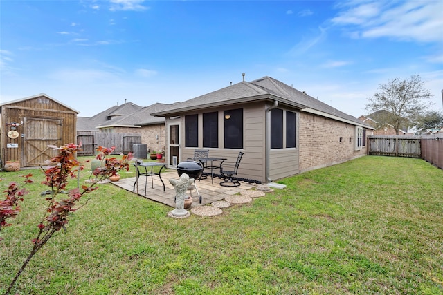 back of property featuring a fenced backyard, a storage unit, a yard, a patio area, and brick siding