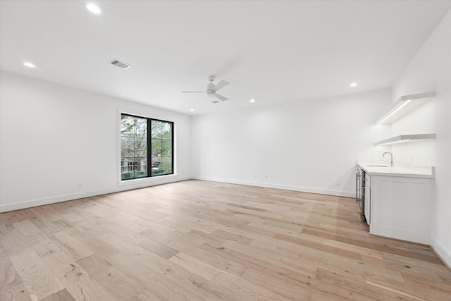 unfurnished living room featuring light hardwood / wood-style floors, ceiling fan, and sink