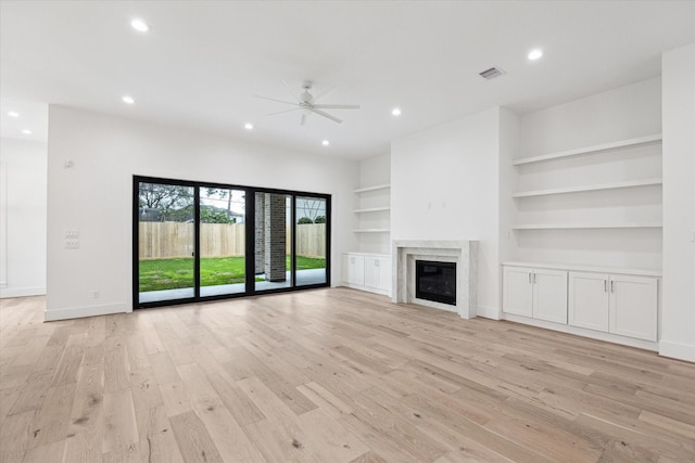 unfurnished living room featuring a fireplace, ceiling fan, built in shelves, and light hardwood / wood-style floors