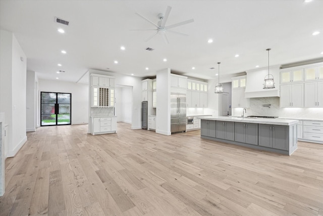 kitchen featuring hanging light fixtures, white cabinets, decorative backsplash, light wood-type flooring, and a large island with sink