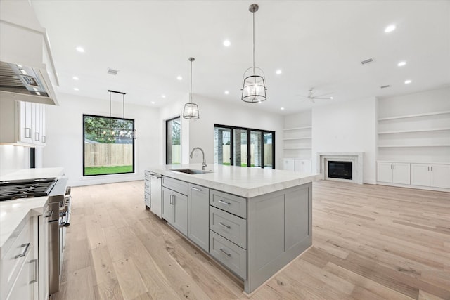 kitchen with a center island with sink, hanging light fixtures, light hardwood / wood-style floors, sink, and built in features