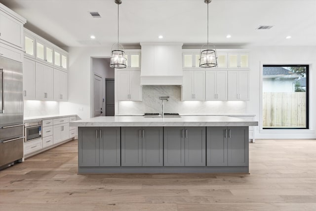 kitchen featuring wall chimney range hood, an island with sink, and gray cabinetry