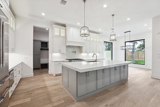 kitchen featuring custom exhaust hood, white cabinets, and a large island with sink