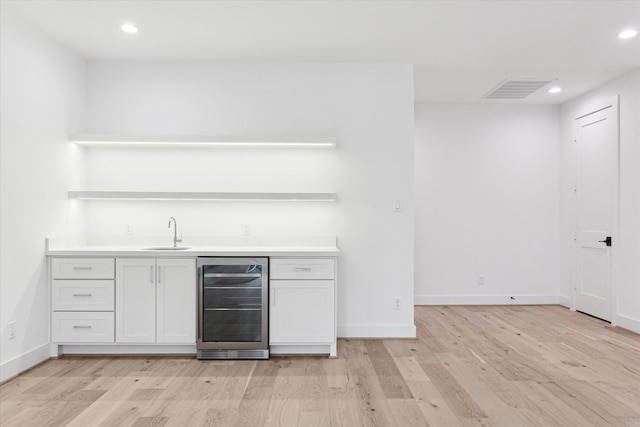 bar with sink, light hardwood / wood-style floors, white cabinets, and wine cooler