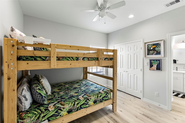 bedroom with sink, light hardwood / wood-style flooring, ceiling fan, ensuite bath, and a closet