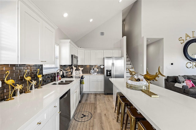 kitchen with a breakfast bar, white cabinetry, sink, stainless steel appliances, and light wood-type flooring