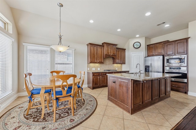 kitchen featuring lofted ceiling, appliances with stainless steel finishes, a kitchen island with sink, light stone countertops, and decorative light fixtures