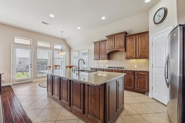 kitchen with sink, hanging light fixtures, light tile patterned floors, appliances with stainless steel finishes, and an island with sink