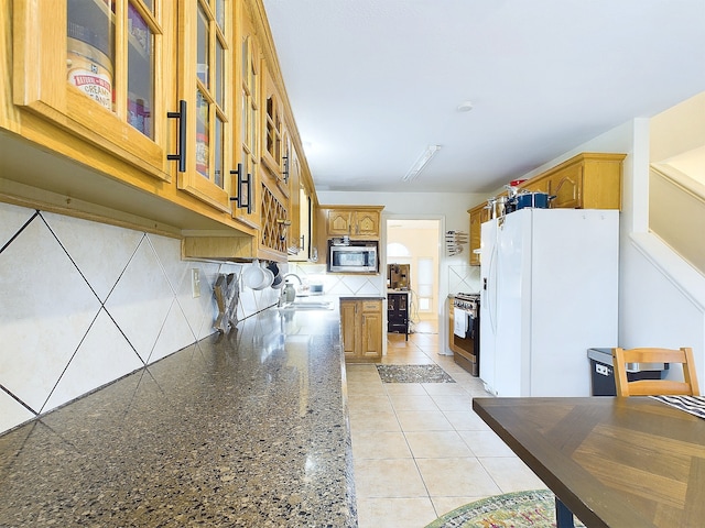 kitchen with glass insert cabinets, appliances with stainless steel finishes, dark stone countertops, brown cabinets, and a sink