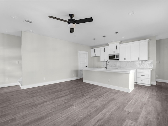 kitchen with decorative light fixtures, white cabinetry, backsplash, dark hardwood / wood-style flooring, and a center island with sink