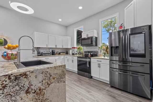 kitchen with sink, light stone counters, appliances with stainless steel finishes, white cabinets, and backsplash