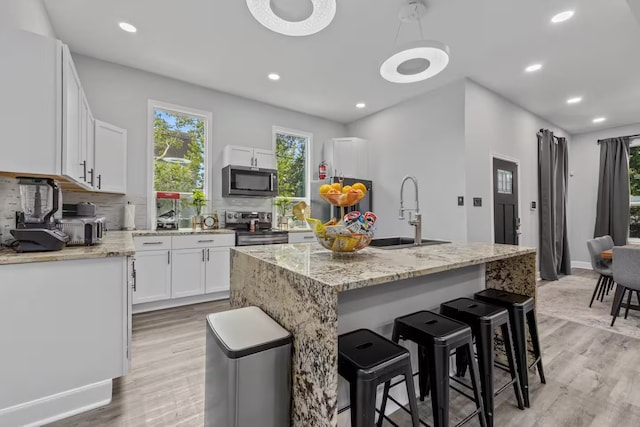 kitchen with sink, appliances with stainless steel finishes, white cabinetry, tasteful backsplash, and a kitchen island