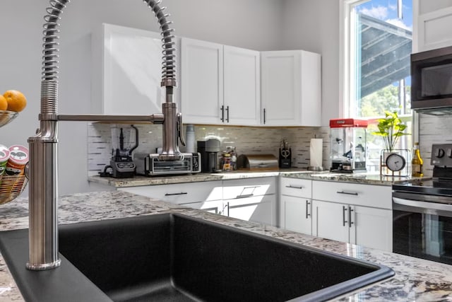 kitchen with light stone counters, backsplash, stainless steel appliances, and white cabinets