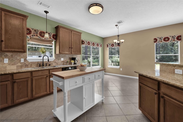 kitchen with sink, light tile patterned floors, hanging light fixtures, backsplash, and wood counters