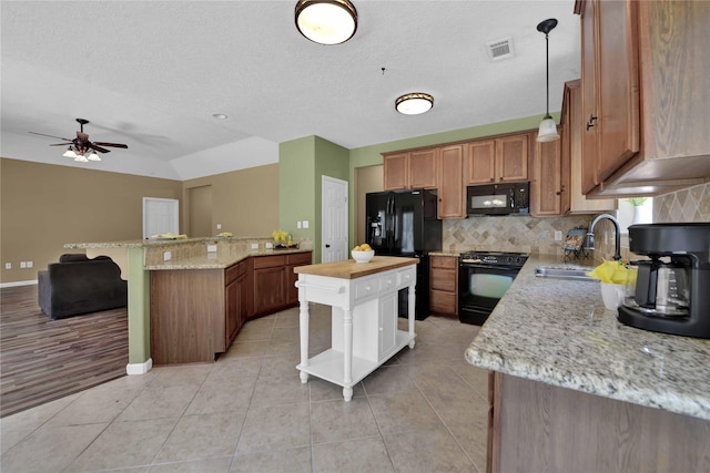 kitchen with a kitchen island, decorative light fixtures, sink, light stone counters, and black appliances