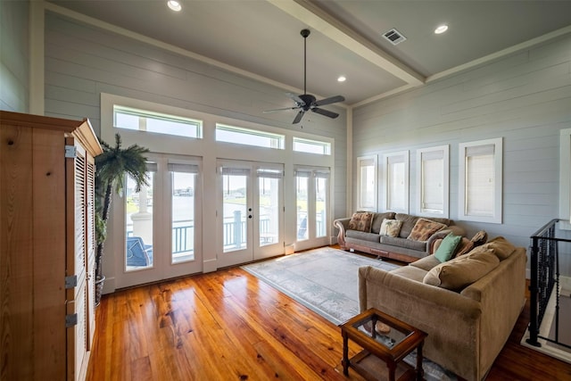 living room with wood walls, beamed ceiling, hardwood / wood-style flooring, ceiling fan, and french doors