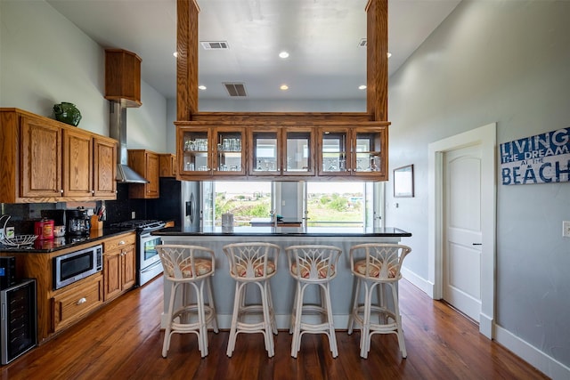 kitchen featuring appliances with stainless steel finishes, a breakfast bar area, beverage cooler, dark hardwood / wood-style flooring, and wall chimney range hood