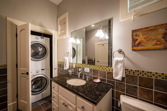 bathroom with toilet, tile walls, vanity, stacked washer / dryer, and tile patterned flooring