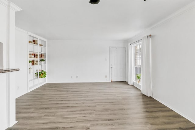 empty room with crown molding, built in shelves, and light hardwood / wood-style flooring