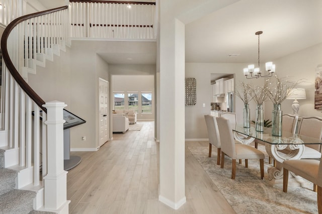 dining area with an inviting chandelier, light hardwood / wood-style flooring, and a high ceiling