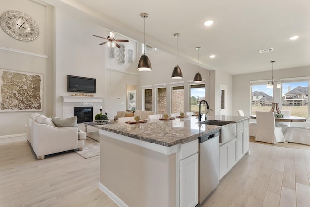 kitchen with white cabinetry, hanging light fixtures, an island with sink, stainless steel dishwasher, and dark stone counters