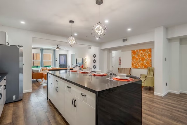 kitchen with dark hardwood / wood-style flooring, stainless steel refrigerator, white cabinets, and a center island with sink