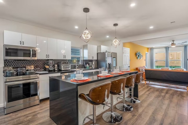 kitchen featuring white cabinetry, light wood-type flooring, a kitchen island, pendant lighting, and stainless steel appliances