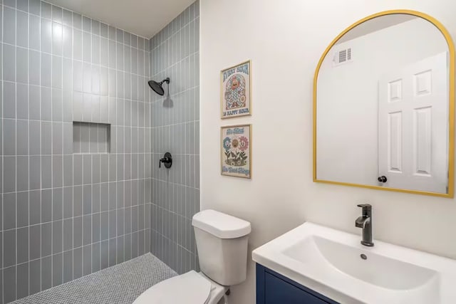 bathroom featuring vanity, a tile shower, and toilet