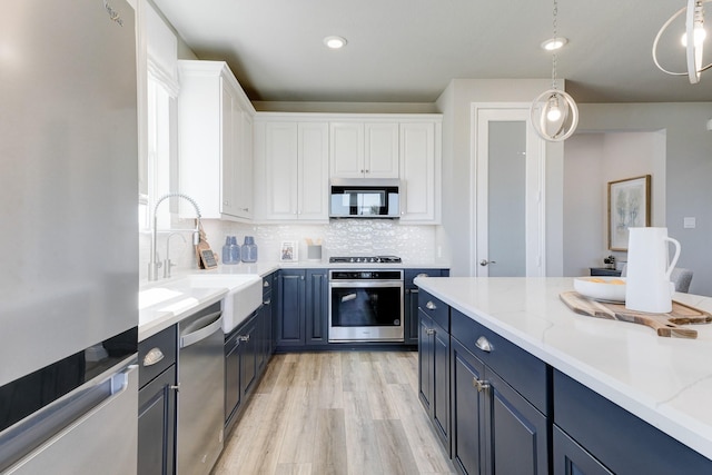 kitchen with tasteful backsplash, a sink, blue cabinets, white cabinetry, and appliances with stainless steel finishes