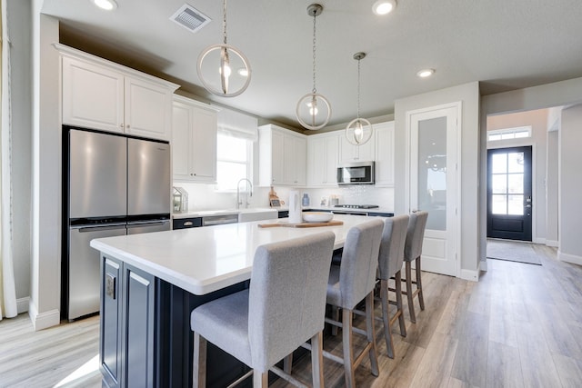 kitchen with a sink, light wood-style flooring, appliances with stainless steel finishes, visible vents, and a kitchen island