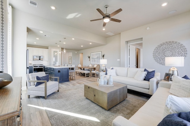 living room featuring light wood finished floors, a ceiling fan, visible vents, and recessed lighting