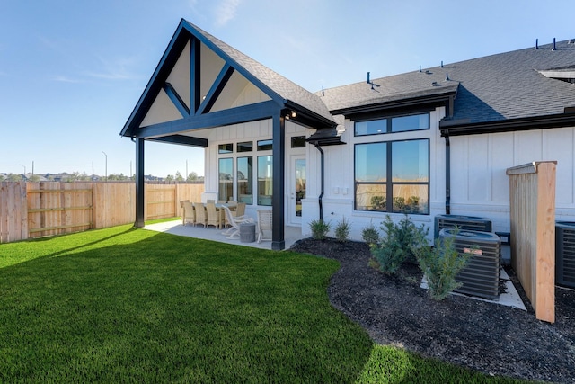 rear view of property with fence, a shingled roof, board and batten siding, a patio area, and a lawn