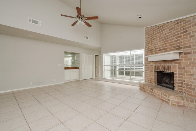 unfurnished living room with ceiling fan, high vaulted ceiling, a brick fireplace, and light tile patterned floors