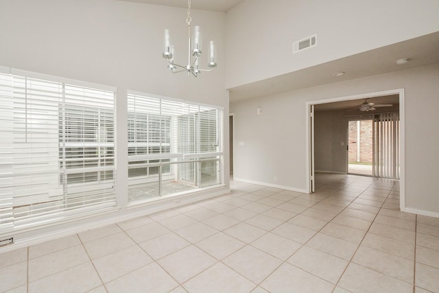 unfurnished dining area with ceiling fan with notable chandelier, a high ceiling, and light tile patterned flooring