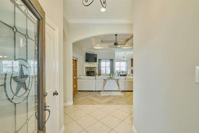 foyer entrance featuring crown molding, a raised ceiling, ceiling fan, a fireplace, and light parquet floors