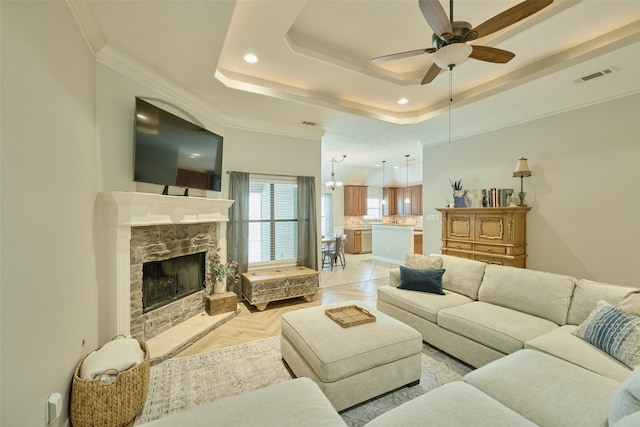 living room featuring light parquet floors, crown molding, a fireplace, and a tray ceiling