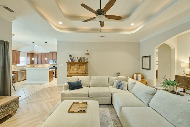 living room with ceiling fan, a tray ceiling, and light parquet floors