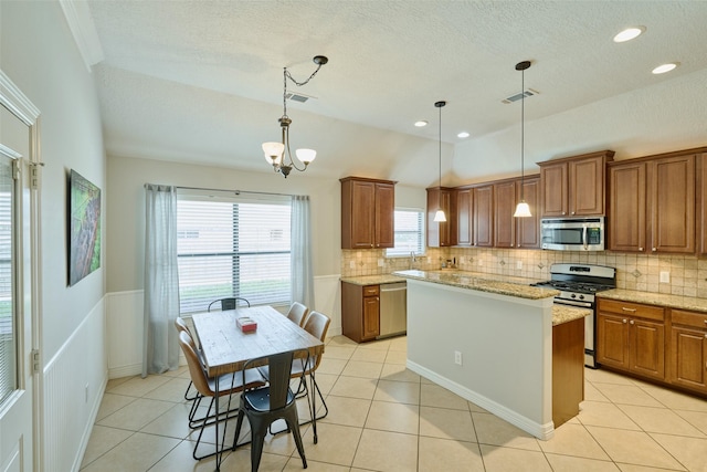 kitchen with a kitchen island, light stone countertops, appliances with stainless steel finishes, and pendant lighting