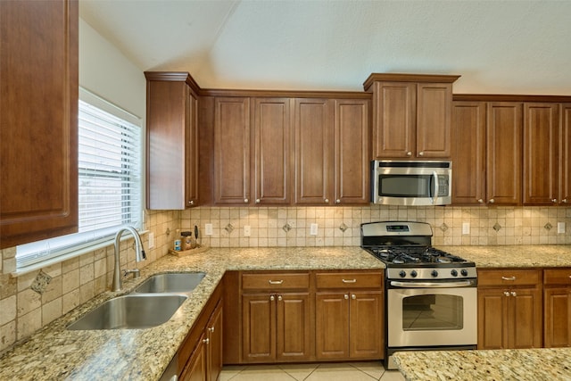 kitchen featuring light tile patterned flooring, sink, light stone counters, stainless steel appliances, and backsplash