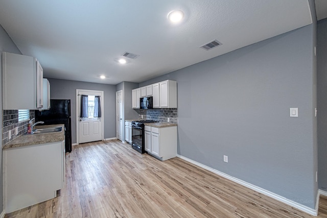 kitchen with tasteful backsplash, white cabinetry, sink, black appliances, and light wood-type flooring