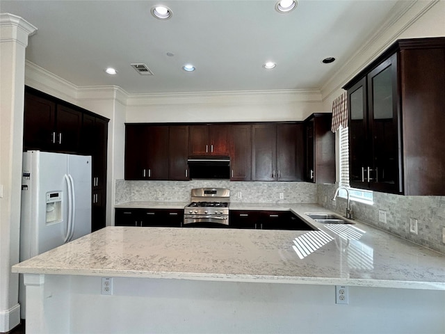 kitchen with sink, stainless steel gas range, white refrigerator with ice dispenser, light stone countertops, and kitchen peninsula