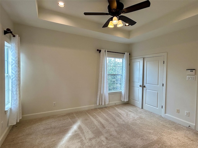 unfurnished bedroom with ceiling fan, light colored carpet, a raised ceiling, and a closet