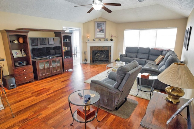 living room with hardwood / wood-style floors, lofted ceiling, a tiled fireplace, ceiling fan, and a textured ceiling