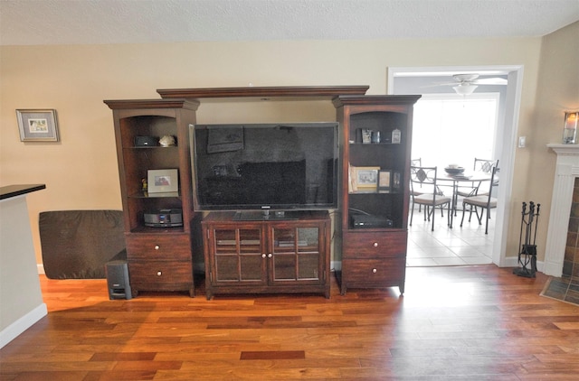 living room with ceiling fan, dark hardwood / wood-style floors, a textured ceiling, and a fireplace