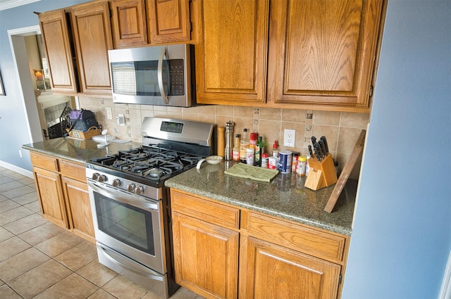 kitchen featuring light tile patterned flooring, appliances with stainless steel finishes, backsplash, and dark stone counters