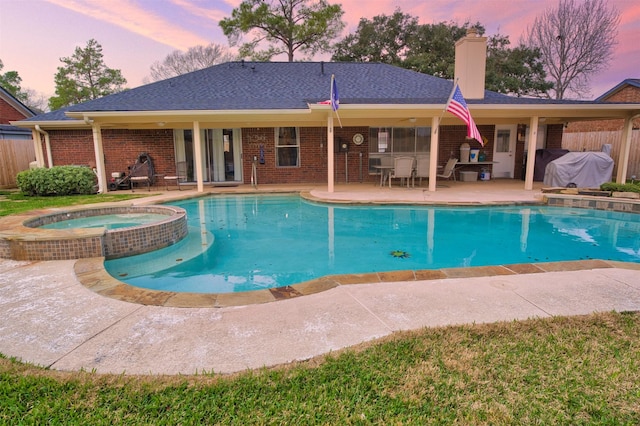 pool at dusk with an in ground hot tub, grilling area, and a patio area