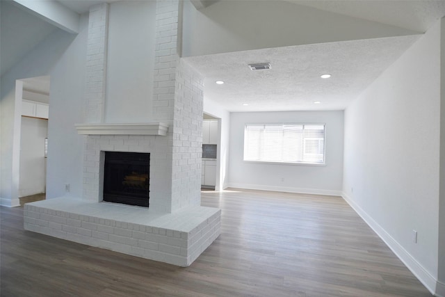 unfurnished living room featuring lofted ceiling, hardwood / wood-style flooring, a fireplace, and a textured ceiling