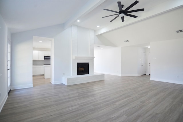 unfurnished living room featuring vaulted ceiling with beams, a fireplace, light hardwood / wood-style floors, and ceiling fan